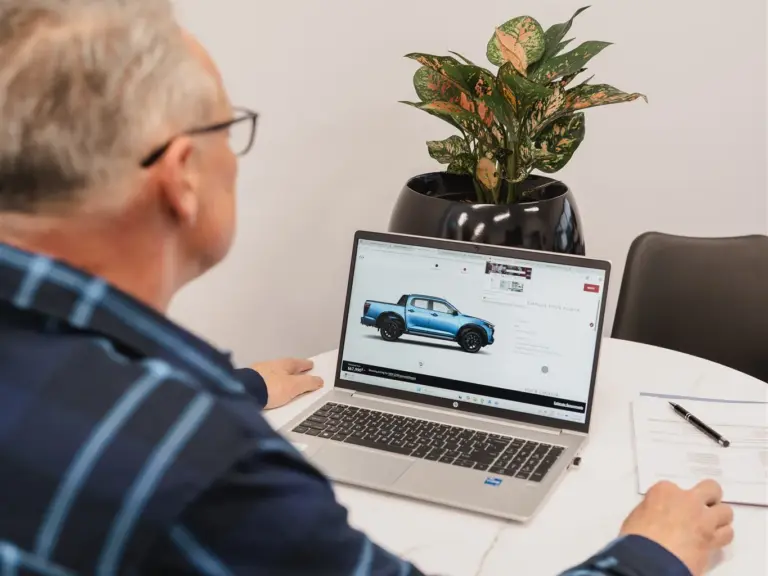 Darren sitting at a desck with his back to us, looking at his laptop, a blue ute on the screen