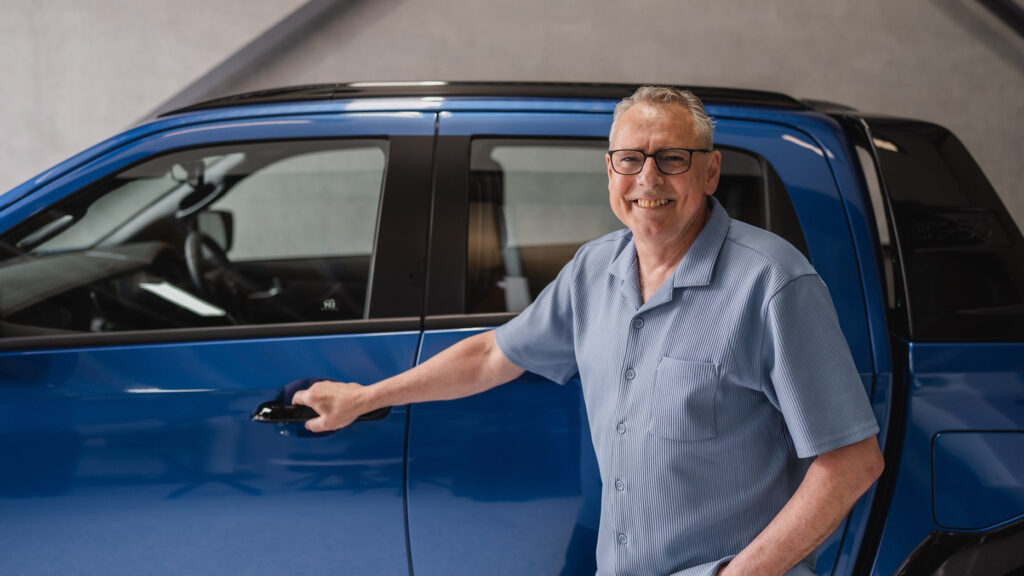 Darren smiling standing against the passenger side of a blue dual cab ute, his hand on the door handle.