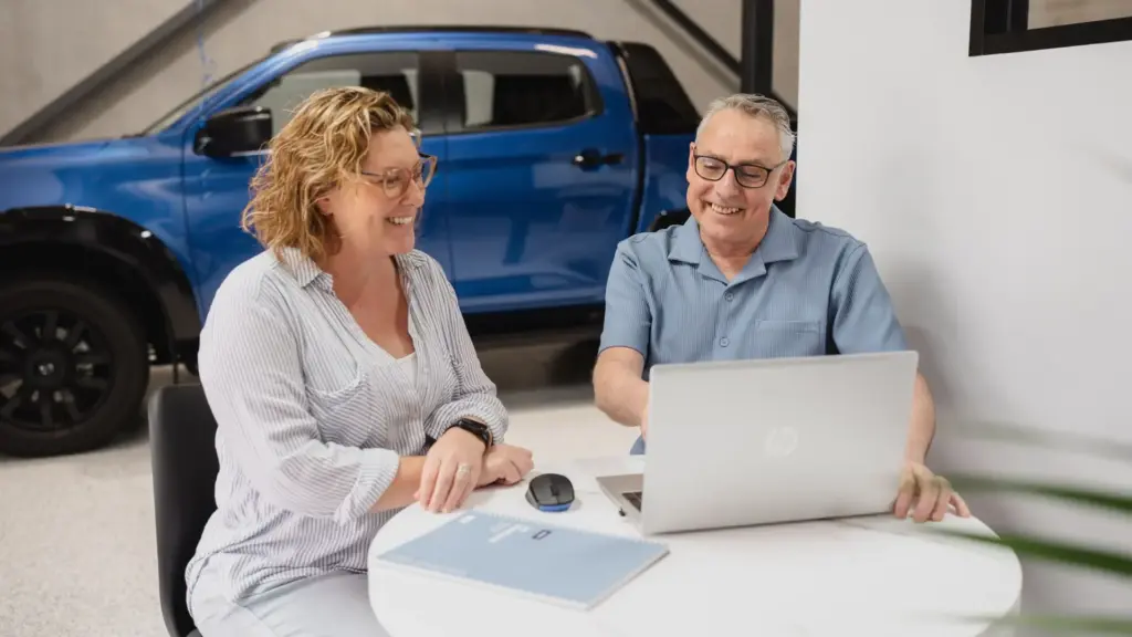 Darren and a client working together, sitting at a small round table, looking at a laptop. A blue dual cab ute is in the background.