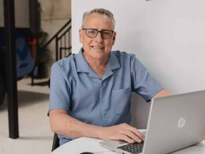 Darren Lewis sitting at a desk with his laptop, looking directly at the camera.